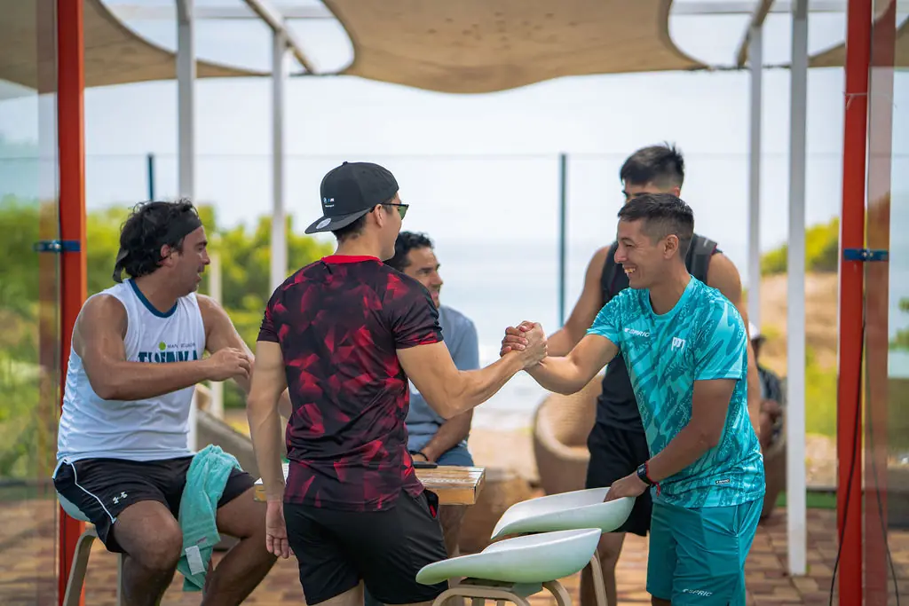 Jugadores saludándose con un apretón de manos y sonriendo, con el mar al fondo