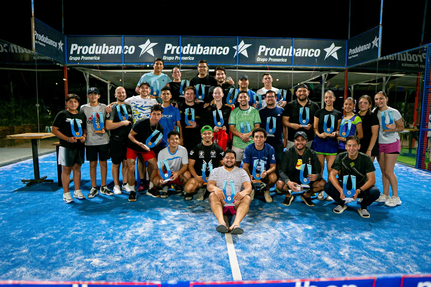 Grupo de campeones posando con sus trofeos después de la premiación de un torneo, bajo las banderolas de Produbanco